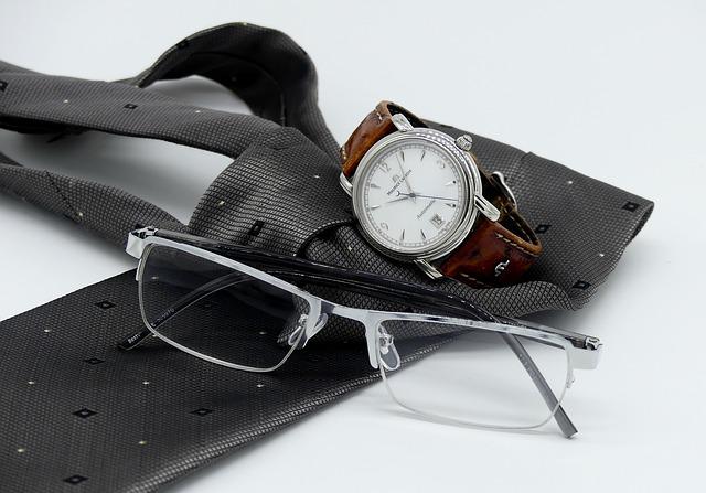Zegarek hybrydowy leży na białym stole obok okularów i krawata