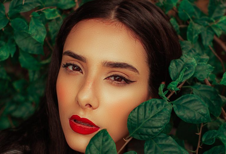 kobieta w mocnym makijażu między zielonymi liśćmi